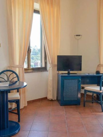 Wohnbereich mit Tisch, Fernseher und Stühlen vor großen Fenstern.