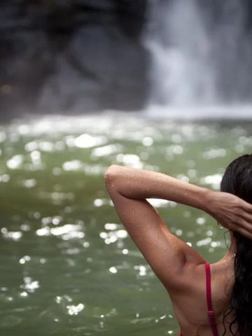 Frau in rotem Badeanzug im Wasser vor einem Wasserfall.