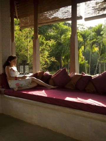 Frau entspannt auf einer Terrasse mit Kissen, umgeben von üppigem Grün.