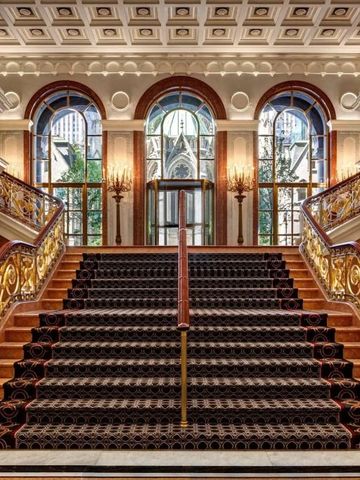 Prächtige Marmortreppe mit verzierten goldenen Geländern und großen Fenstern.