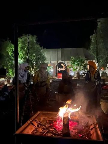 Lagerfeuer in einem Camp umgeben von Menschen bei Nacht