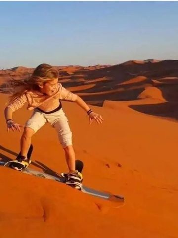 Person beim Sandboarden auf beeindruckenden Wüstendünen bei Sonnenuntergang