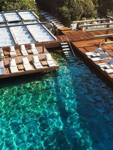 Sonniger Außenpool mit Holzdeck und Liegeflächen am kristallklaren Wasser