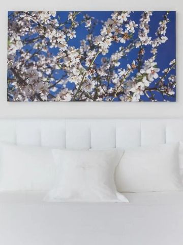 Kunstwerk mit Blütenmotiv über einem weißen Bett in einem Hotelzimmer