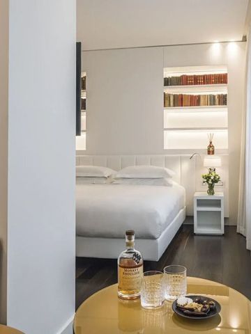 Hotelzimmer mit Bücherregal, weißem Bett und Tisch mit Getränken