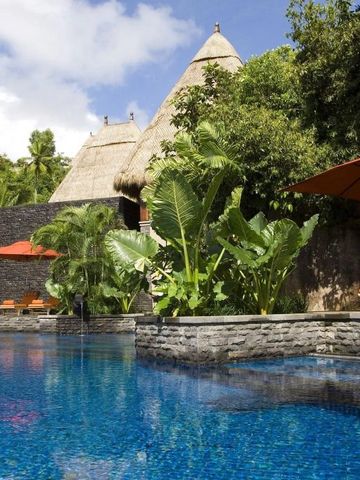 Infinity Pool umgeben von üppiger Pflanzenwelt und Strandhütten