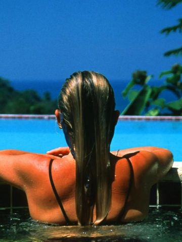 Frau entspannt am Rand eines Infinity Pools mit Meerblick