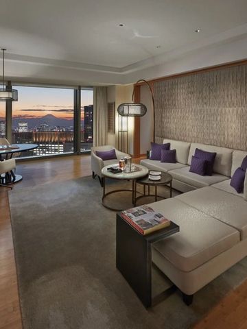 Großzügige Suite mit Sitzbereich und Panoramablick auf die Stadt bei Sonnenuntergang