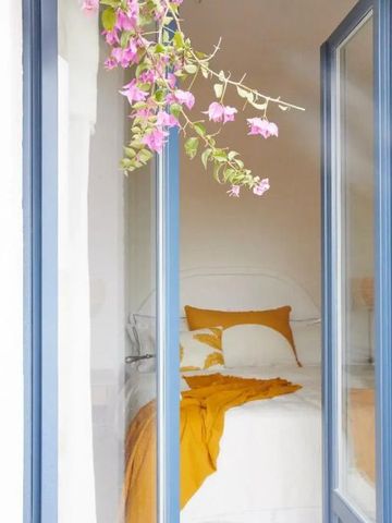 Gemütliches Bett mit gelber Dekoration hinter großen Fenstern mit Blumen.