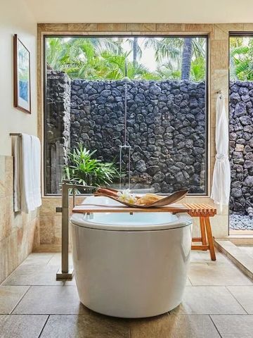 Luxuriöses Badezimmer mit freistehender Badewanne und Blick auf tropischen Garten