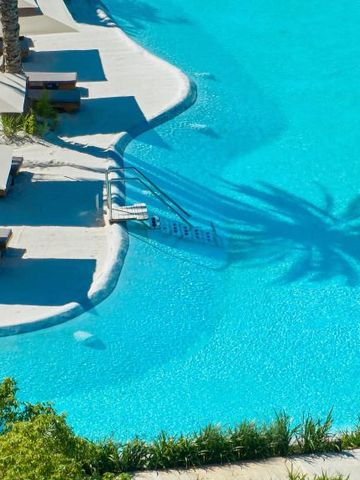 Sonnenliegen und Palmenschatten an einem türkisfarbenen Pool