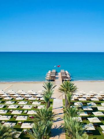Weißer Sandstrand mit gepflegten Liegen und einem Holzsteg am türkisblauen Meer
