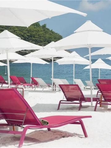 Weißer Sandstrand mit rosa Liegen und Sonnenschirmen vor blauem Meer