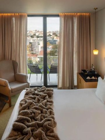 Elegantes Zimmer mit Doppelbett, Sessel und Blick auf die Stadt durch große Fenster