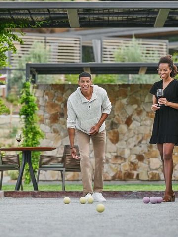 Pärchen spielt Boule neben einer modernen Terrasse mit Wein.