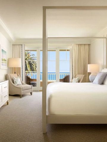 Helles Hotelzimmer mit Himmelbett und Blick auf das Meer von einem Balkon.