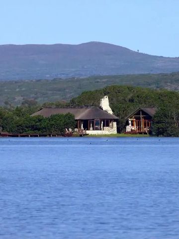 Blick auf Lodges am Ufer eines großen Gewässers mit Hügeln im Hintergrund