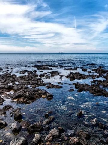 Steiniger Strand mit Blick auf das ruhige blaue Meer und einem klaren Himmel