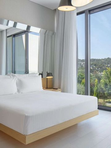 Helles Gästezimmer mit weißem Bett und großen Fenstern mit Gartenblick