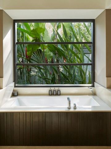 Elegantes Badezimmer mit großer Badewanne und Blick auf tropische Pflanzen