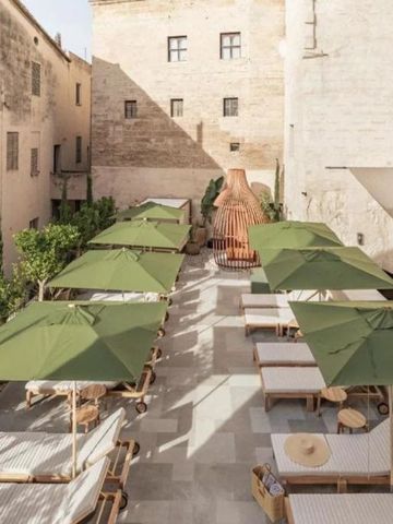 Sonnenterrasse mit Liegestühlen und grünen Sonnenschirmen zwischen historischen Mauern