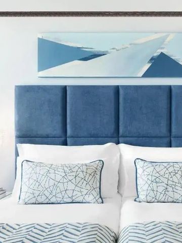 Elegantes Hotelzimmer mit blauem Kopfteil und moderner Kunst.