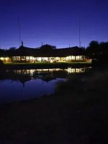 Nachtaufnahme des Okonjima Luxury Bush Camp mit Reflexion im Wasser.