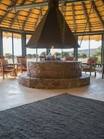 Großer Kamin mit Sitzgelegenheiten unter einem strohgedeckten Dach im Okonjima Luxury Bush Camp.
