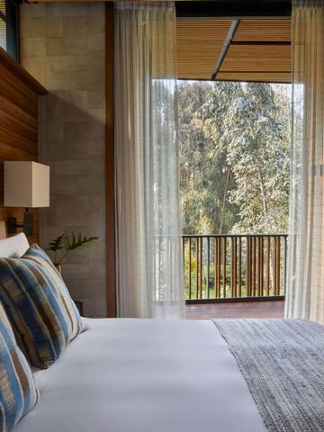 Helles Schlafzimmer mit großem Fenster und Ausblick auf bewaldete Landschaft