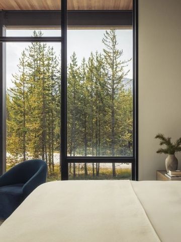 Zimmer mit großer Fensterfront und Aussicht auf einen Wald und Berge im Hintergrund.