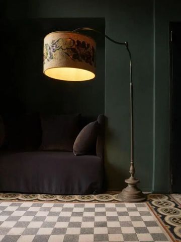 Gemütlicher Loungebereich mit Sofa und dekorativer Stehlampe vor dunkelgrüner Wand.