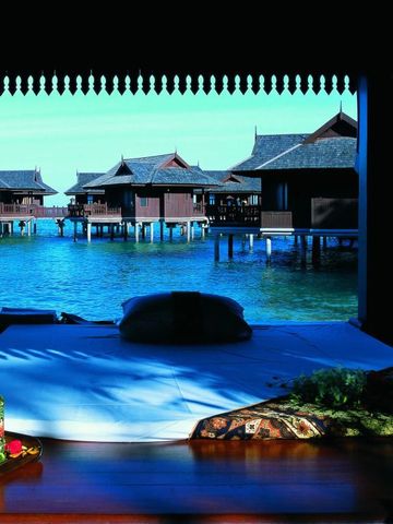 Blick von einem Wasser-Bungalow auf das glitzernde Meer und angrenzende Villen