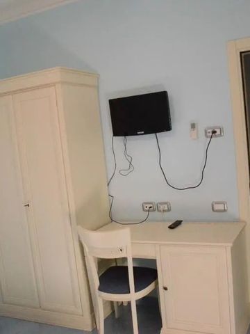 Einfach eingerichtetes Hotelzimmer mit Schreibtisch, Stuhl, Kleiderschrank und Fernseher