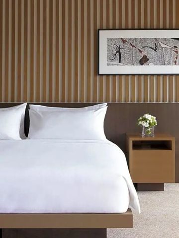 Helles Doppelbett mit dekorativer Wandkunst und Nachttisch mit Blumen.