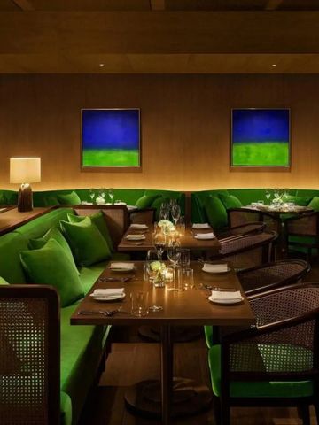 Elegantes Restaurant mit grünen Samtsofas und Kunstwerken an den Wänden