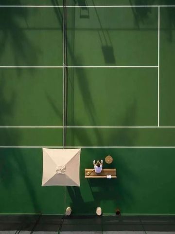 Person sitzt unter Sonnenschirm auf einem Tennisplatz