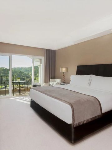 Elegantes Schlafzimmer mit großem Bett und Balkonaussicht auf grüne Landschaft