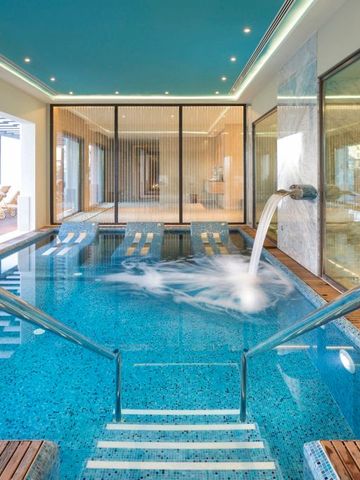 Innenpool mit Wasserstrahl und Glaswänden im Wellnessbereich.