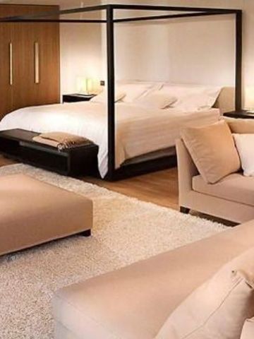 Geräumige Hotelsuite mit Himmelbett und hellen Möbeln auf einem Teppichboden.