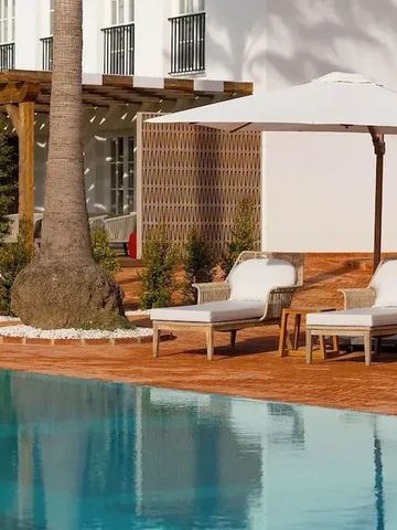 Poolbereich mit bequemen Sonnenliegen und Sonnenschirm neben Palmen.