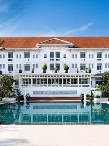Fassade des Raffles Grand Hotel d'Angkor mit großem Pool im Vordergrund und hellem Himmel