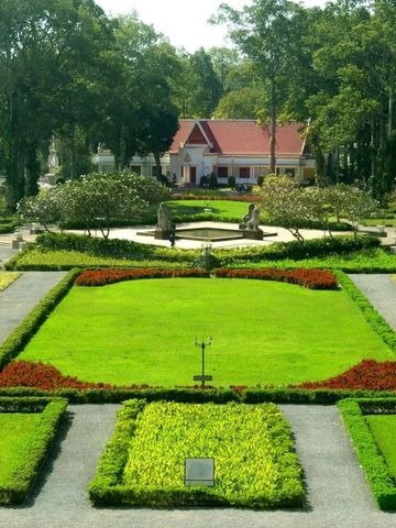 Üppiger grüner Garten mit symmetrischen Hecken und einem kleinen Gebäude im Hintergrund