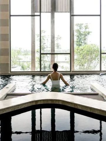 Frau entspannt im Innenpool mit Blick auf grüne Landschaft durch große Fenster