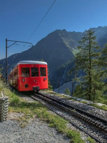 Roter Bergzug fährt auf einer schmalen Schiene mit Blick auf beeindruckende Berge.
