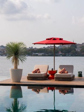 Liegestühle und roter Sonnenschirm am Rixos Tersane Pool mit Blick auf Wasser.