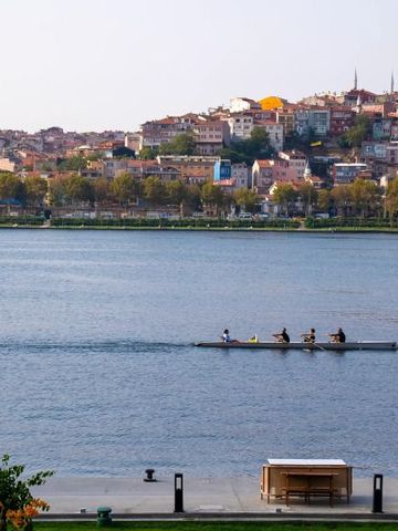 Blick auf einen Fluss mit Ruderboot und Wohngebäude im Hintergrund.