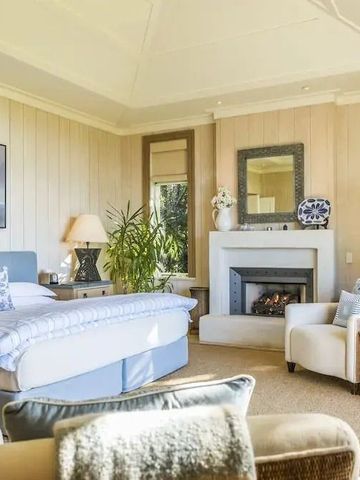Helles Hotelzimmer mit Kamin, gemütlichen Sesseln und großen Fenstern mit Gartenblick