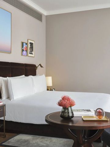 Modernes Hotelzimmer mit gemütlichem Bett, Kunstwerken und frischen Blumen auf dem Tisch.