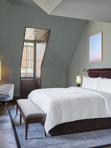 Dachzimmer mit gemütlichem Bett, schräger Decke und Sitzbereich neben dem Fenster.