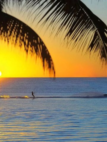 Spektakulärer Sonnenuntergang über dem Ozean mit Palmen und Wassersportler